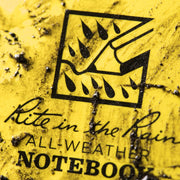 Yellow notebook cover with black text and symbol, indicating 'All-Weather Notebook'. mud on cover