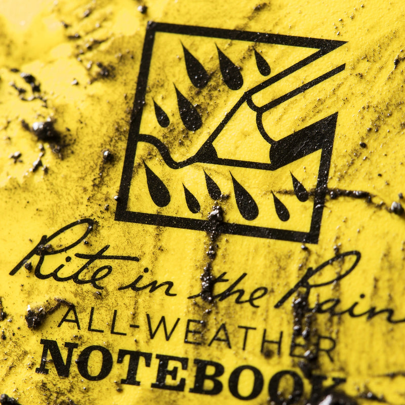 Yellow notebook cover with black text and symbol, indicating 'All-Weather Notebook'. mud on cover