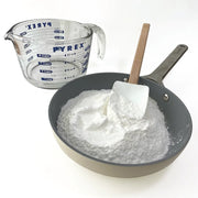 Pyrex measuring cup next to a pan with dough mix and a spatula on a white background