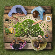 Four people working on a large oak tree puzzle at a wooden table outdoors.