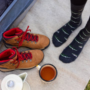 Hiking boots, fish socks, and a cup of tea on a camping mat.