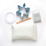 Snowflake cookie cutter, ribbon, bag of glitter with a hole puncher, container, and bag of white dough mix on a white background