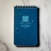 Blue notebook with 'Rite in the Rain' branding on a marble surface