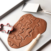 salt dough with gingerbread man shapes on a baking tray, with a cookie cutter and rolling pin.