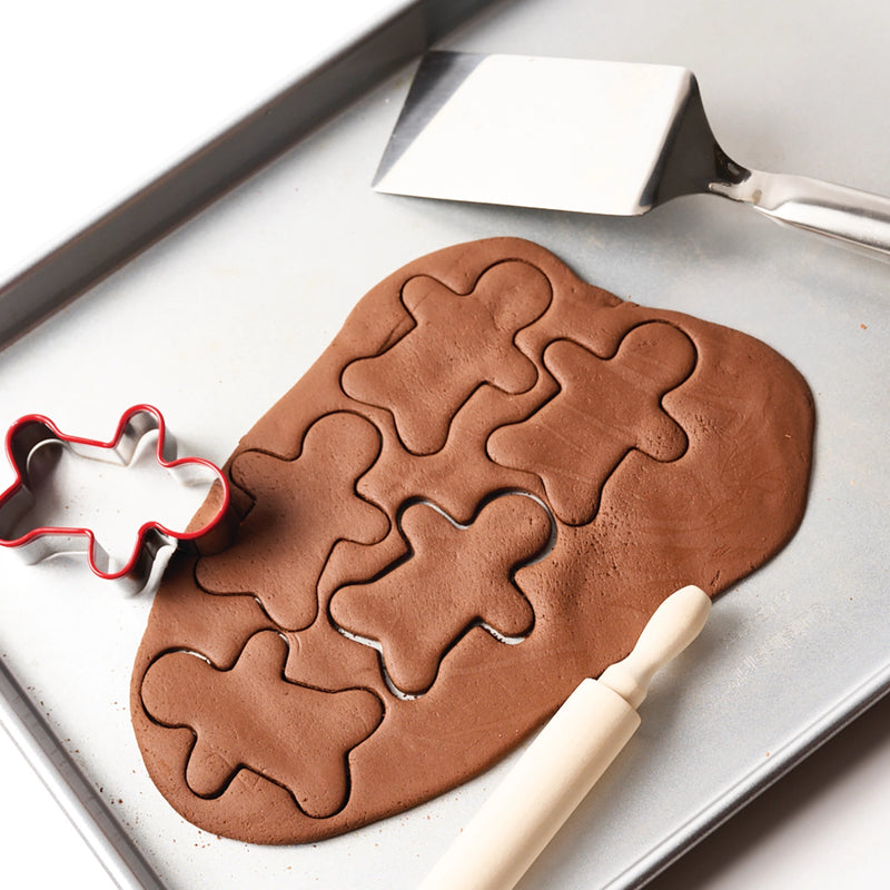 salt dough with gingerbread man shapes on a baking tray, with a cookie cutter and rolling pin.