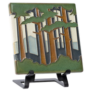Decorative tile with forest and mountain design on a metal easel 