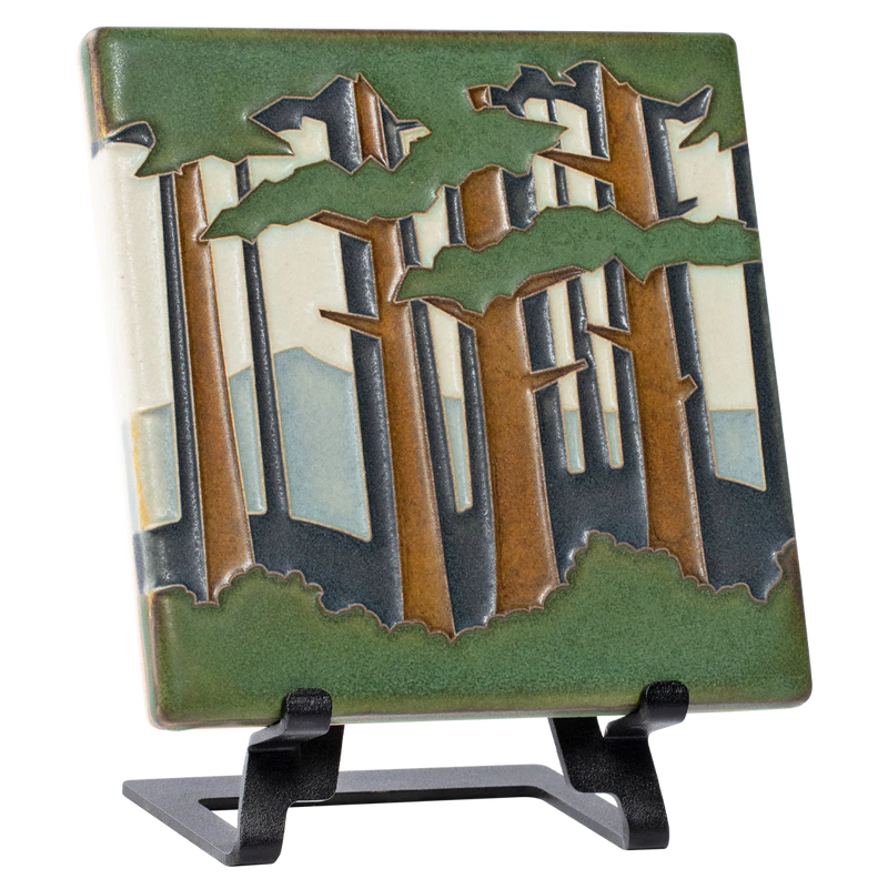 Decorative tile with forest and mountain design on a metal easel 