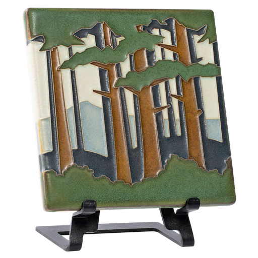 Decorative tile with forest and mountain design on a metal easel 