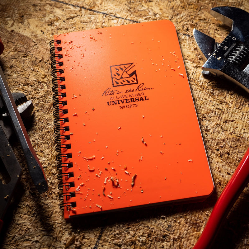 Orange notebook with 'Rite in the Rain' logo on a textured surface with tools.