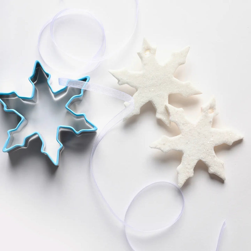 Snowflake cookie cutter and white snowflake-shaped cookie on a light background