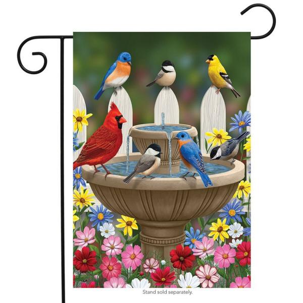 three chickadees, two bluebirds, a cardinal and a goldfinch gathered around a two tiered fountain surrounded by colorful flowers and a fence
