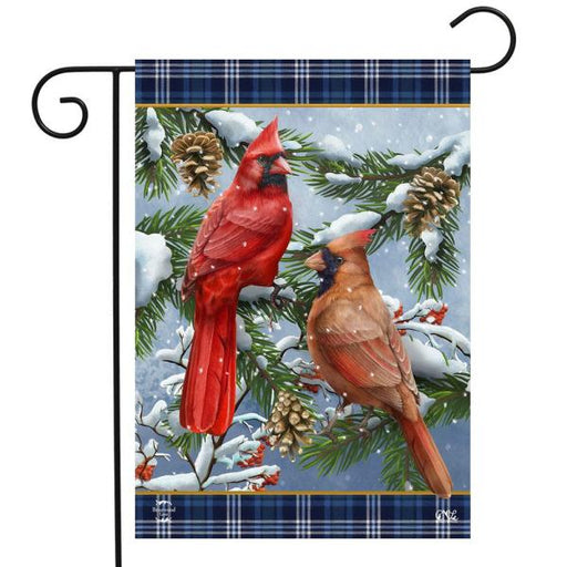a pair of cardinals perched in a snowy evergreen tree surrounded by some pinecones. top and bottom border is a dark blue and white plaid pattern