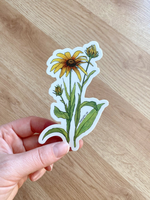 Hand holding a sticker of a black eyed susan wildflower with green leaves 