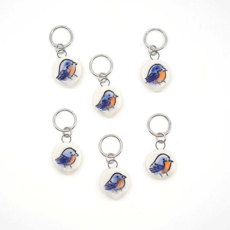 Set of six bluebird-themed ceramic stitch markers on a white background