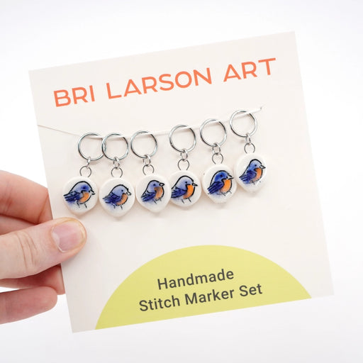 Handmade ceramic stitch marker set with bluebird design on a Bri Larson Art branded card.