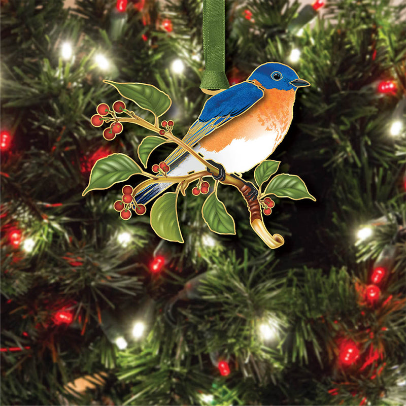 Decorative ornament featuring a bluebird on a branch with berries on a holiday tree with lights.