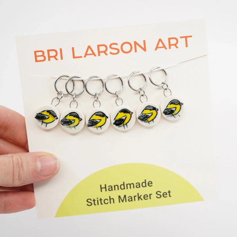 Handmade ceramic stitch marker set with goldfinch design on a Bri Larson Art branded card.