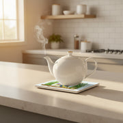 White teapot with steam on a kitchen counter protected by trivet