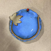 Blue ceramic dish with moonseed leaf and ladybug design on a beige background