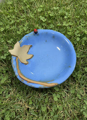 Ceramic bowl with blue glaze with a decorative moonseed vine leaf and a ladybug sitting in the grass