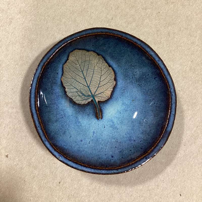 Blue ceramic bowl with an embossed  leaf on a beige background