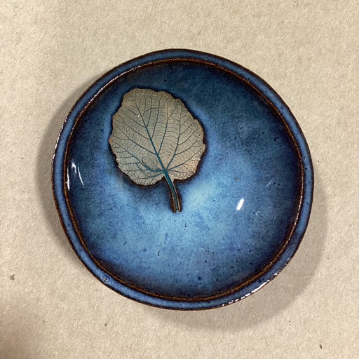 Blue ceramic bowl with an embossed  leaf on a beige background