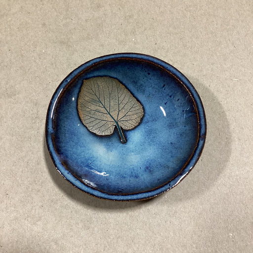 Blue ceramic bowl with a leaf on a beige background