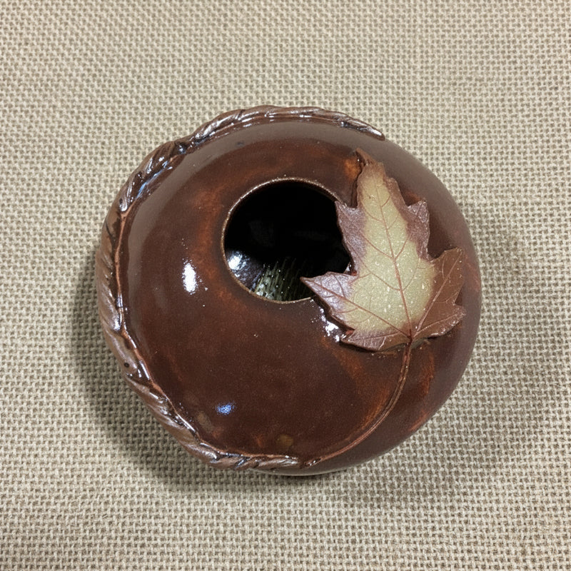 Brown ceramic pillow vase with a maple leaf on top