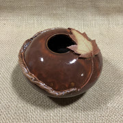 Brown ceramic vase with maple leaf design on jute background