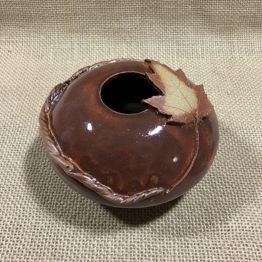 Brown ceramic vase with maple leaf design on jute background