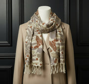 Draped scarf with leaf pattern on a mannequin with a beige coat and dark background