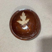 Brown ceramic bowl with a leaf design on a beige background