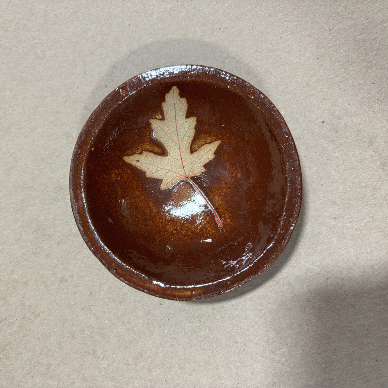 Brown ceramic bowl with a leaf design on a beige background