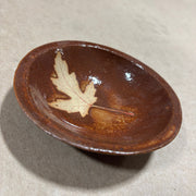Brown ceramic dish with a leaf design on a beige background