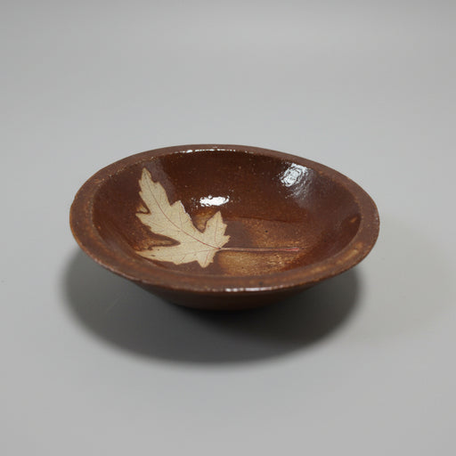 Brown ceramic dish with a leaf design on a beige background