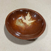 Brown ceramic dish with a leaf design on a beige background
