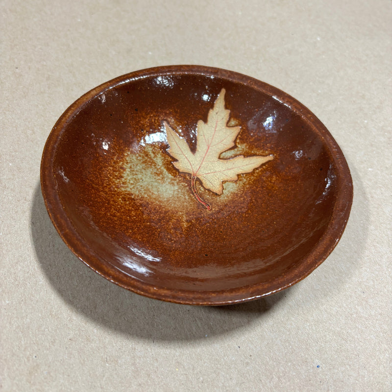 Brown ceramic dish with a leaf design on a beige background