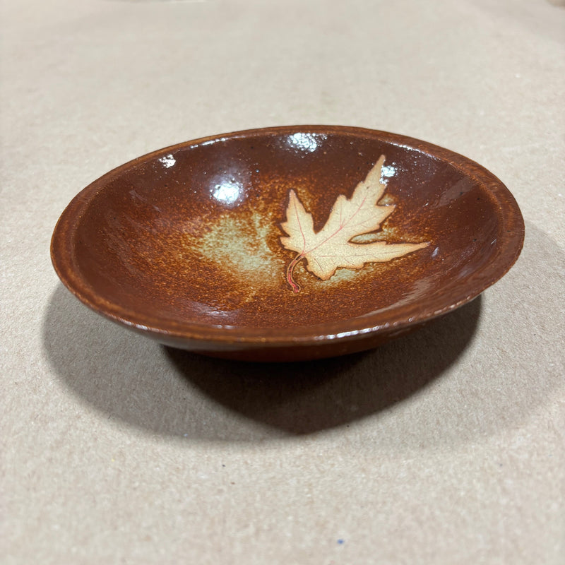 Brown ceramic bowl with a leaf design on a beige surface