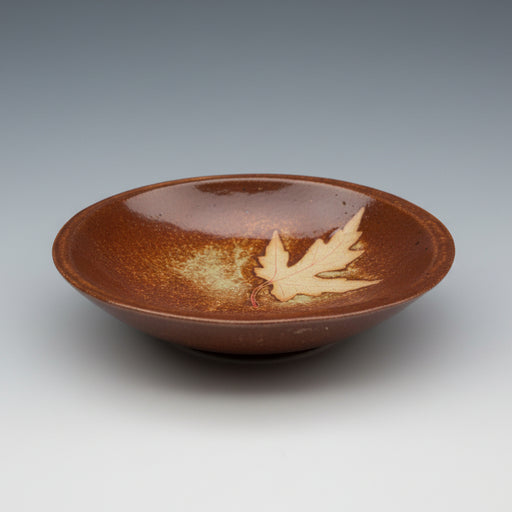 Brown ceramic bowl with a leaf design on a beige surface