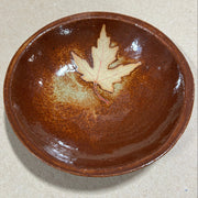 Brown ceramic bowl with a leaf design on a beige background