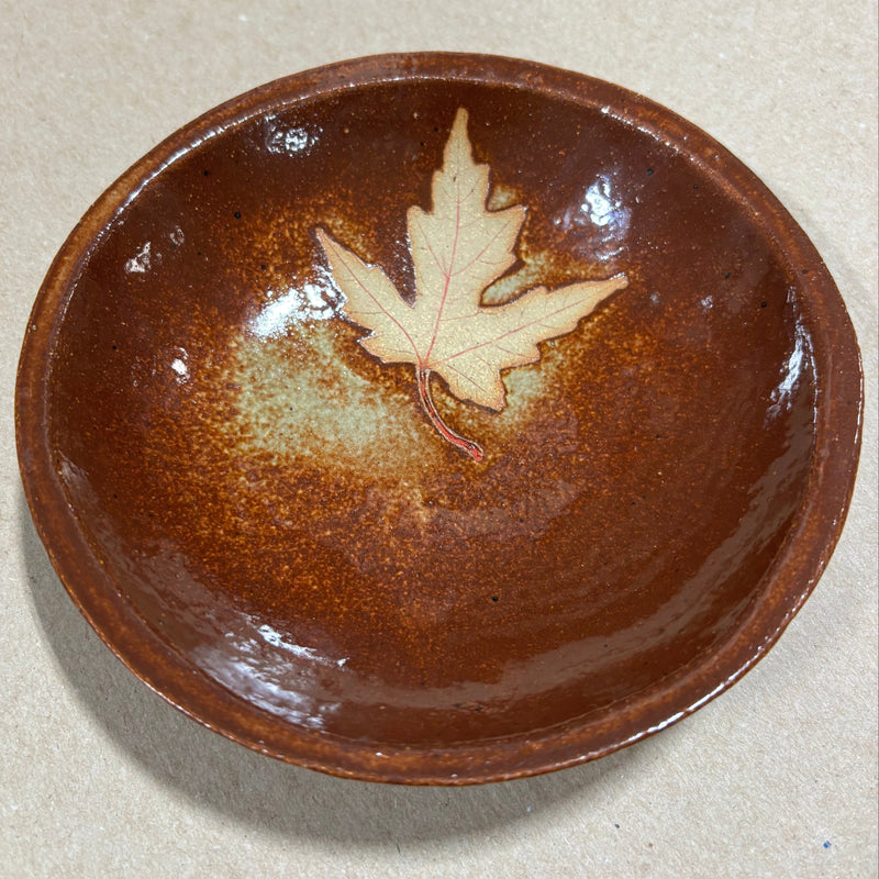 Brown ceramic bowl with a leaf design on a beige background