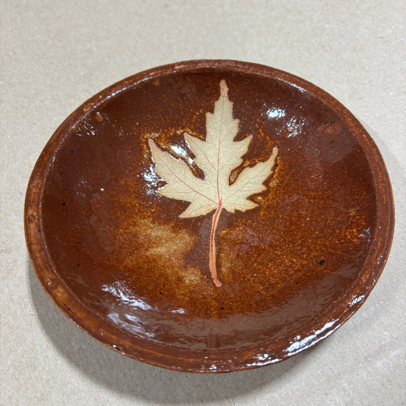 Brown ceramic plate with a leaf design on a beige background