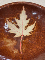 close up of a brown ceramic plate with a leaf on a textured surface