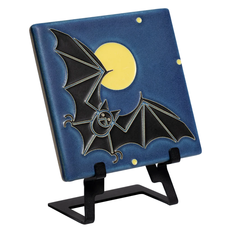 Decorative tile with a black bat design displayed on a metal easel 