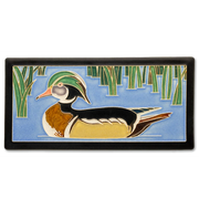 Decorative tile with a wood duck design on a blue water background with green reeds.
