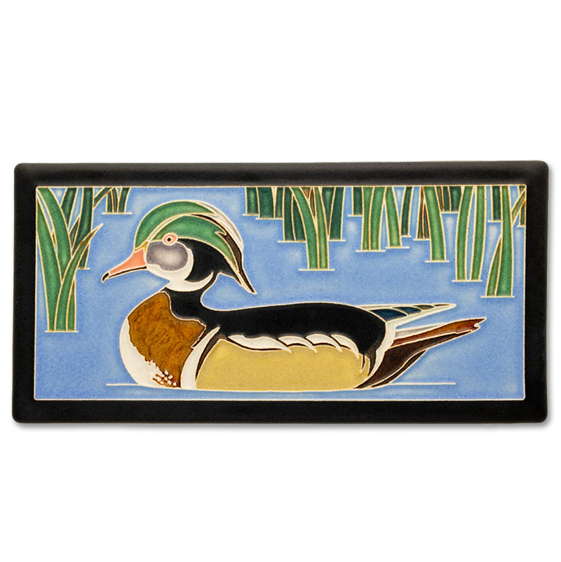 Decorative tile with a wood duck design on a blue water background with green reeds.