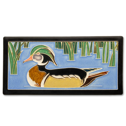 Decorative tile with a wood duck design on a blue water background with green reeds.
