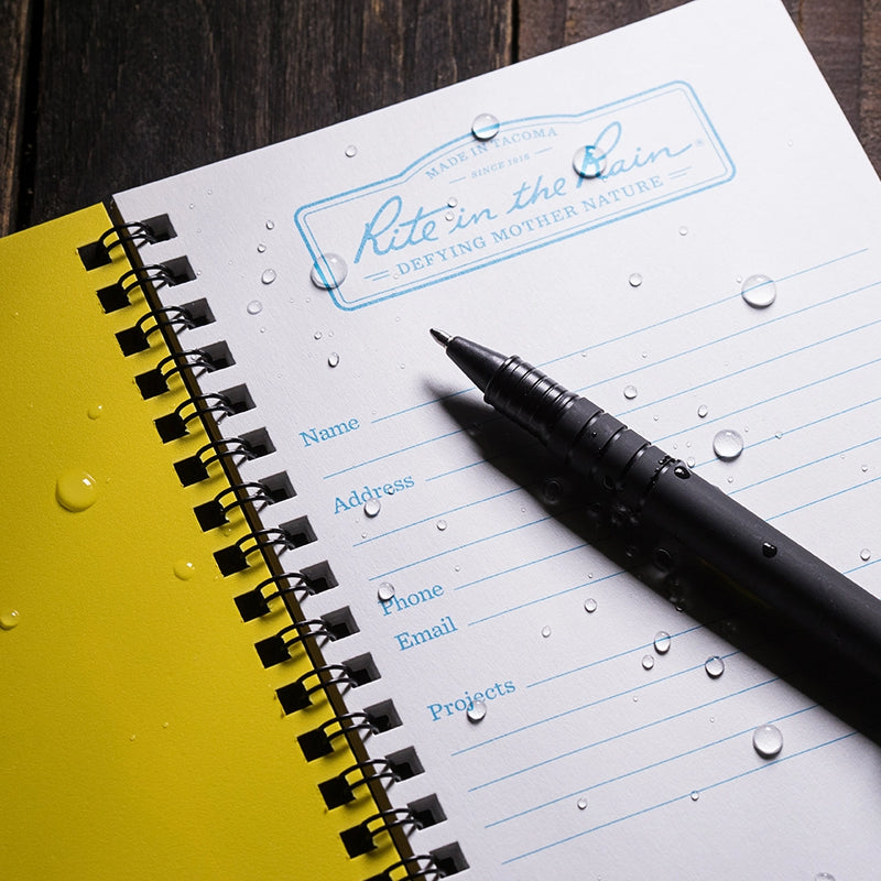 Notebook with a pen and water droplets on paper surface, featuring 'Rite in the Rain' branding.