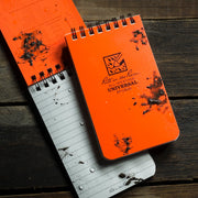 Orange notebooks with 'Rite in the Rain' logo covered in mud and splashed with water