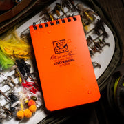 Orange notebook with 'Rite in the Rain' logo on a background of fishing equipment